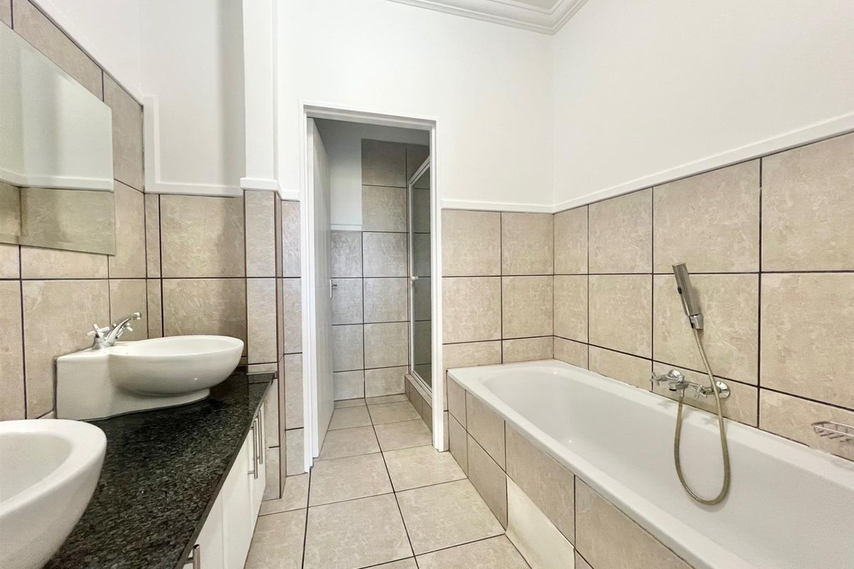 A well-maintained bathroom featuring a double vanity with granite countertops, a bathtub with a handheld shower attachment, and neutral wall tiling.