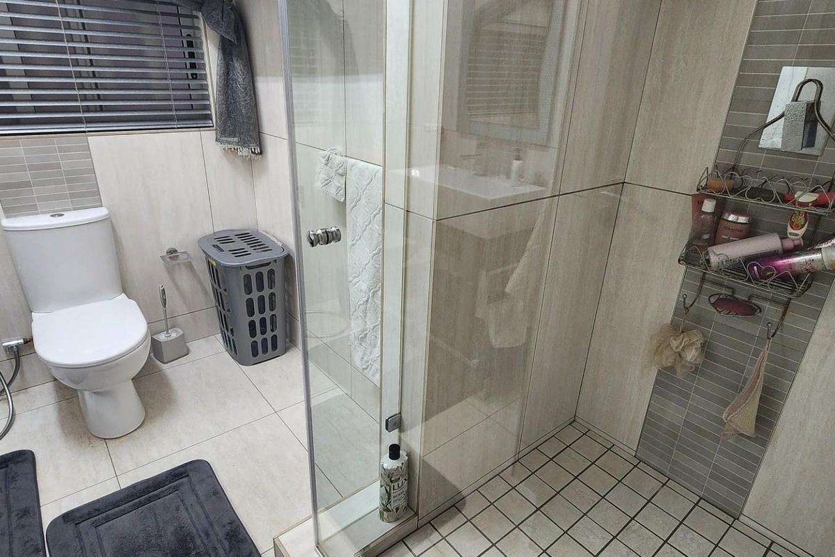 Modern bathroom featuring a glass-enclosed shower, tiled walls, and a standard toilet suite with a bidet spray attachment.