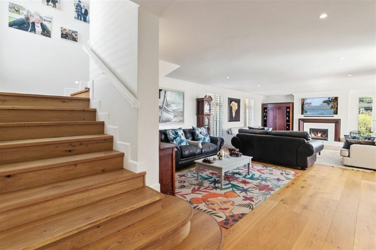 Spacious living room featuring hardwood flooring, a fireplace, and a timber staircase leading to the upper level, complemented by recessed lighting and plantation shutters.