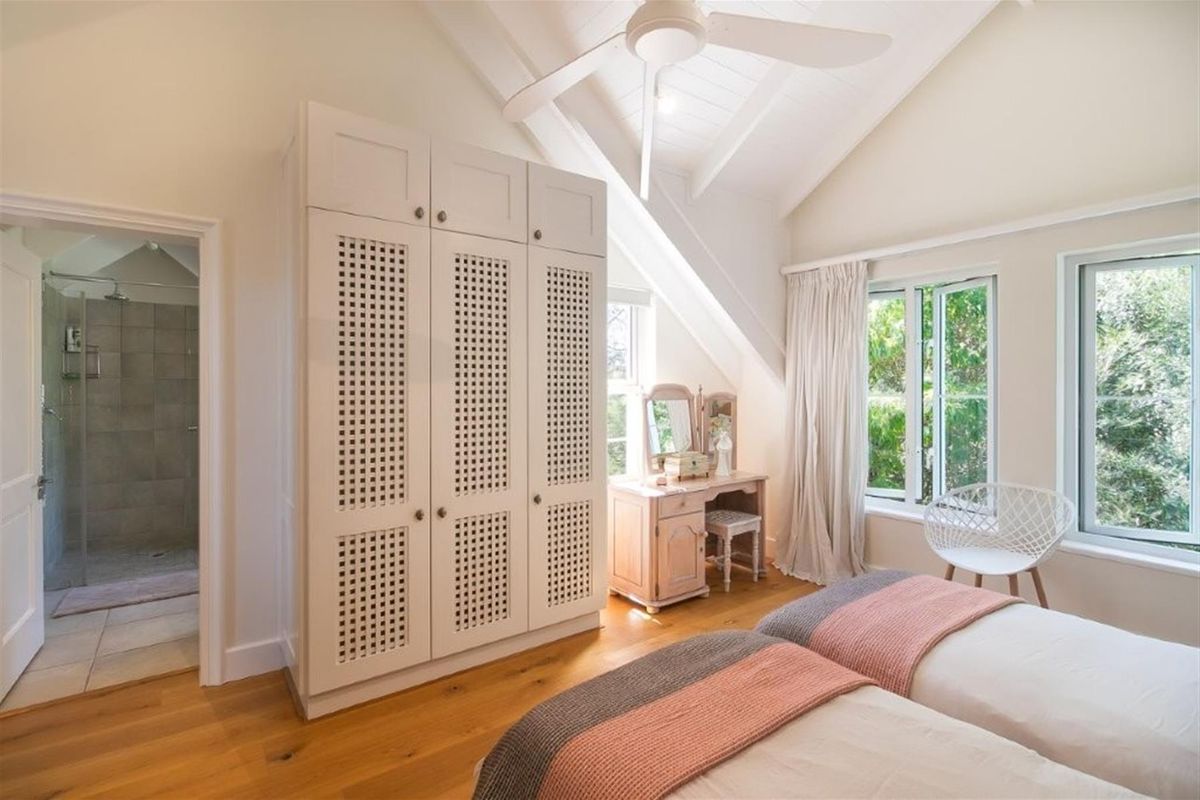 Bright bedroom featuring vaulted ceilings, ceiling fan, hardwood flooring, built-in wardrobe, and direct access to an en-suite bathroom.