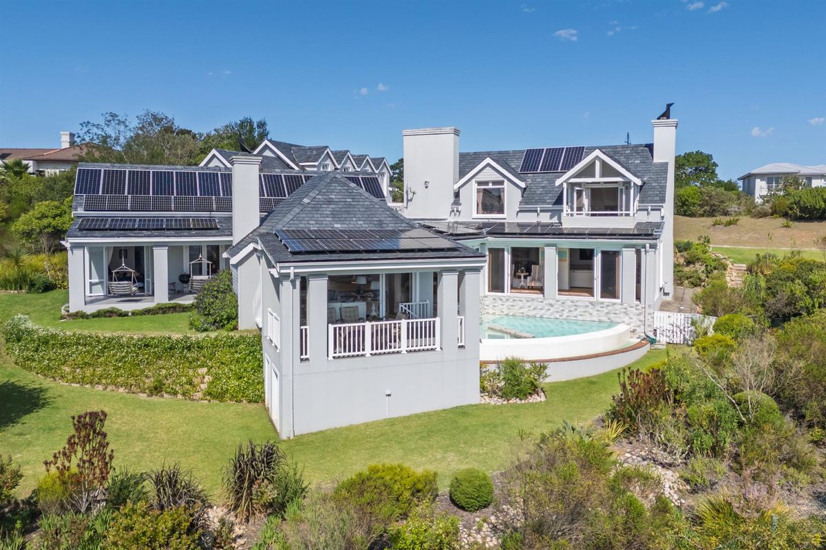 Aerial view of the rear elevation featuring a swimming pool, extensive solar panel installation, slate roofing, and a well-maintained landscaped garden.