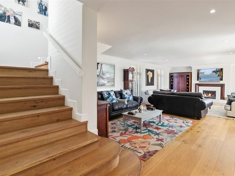 Spacious living room featuring hardwood flooring, a fireplace, and a timber staircase leading to the upper level, complemented by recessed lighting and plantation shutters.