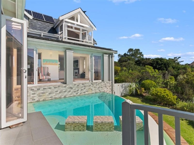 A beautiful outdoor pool area featuring an infinity edge pool, stone accents, and seamless indoor-outdoor flow through large bi-fold doors.