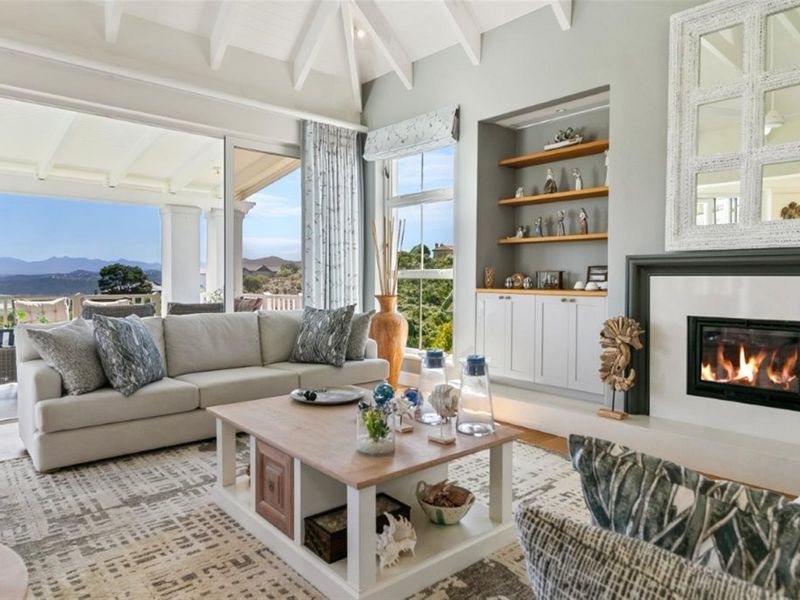 Bright living room featuring a vaulted ceiling with exposed rafters, a built-in fireplace, custom cabinetry, and large sliding doors opening to a scenic patio.
