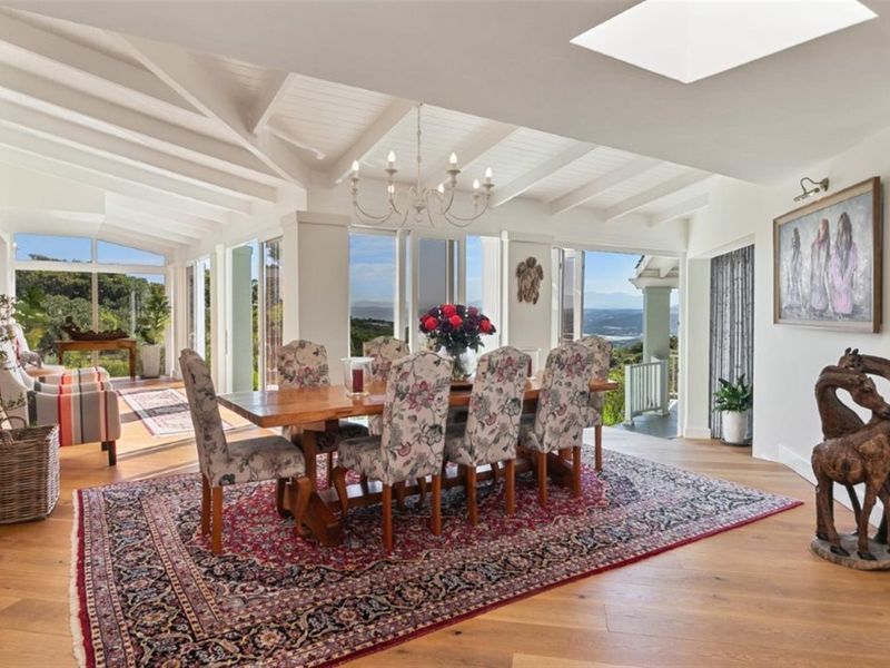 Spacious dining area featuring exposed timber ceiling beams, a large skylight, hardwood flooring, and expansive glass doors offering scenic views.