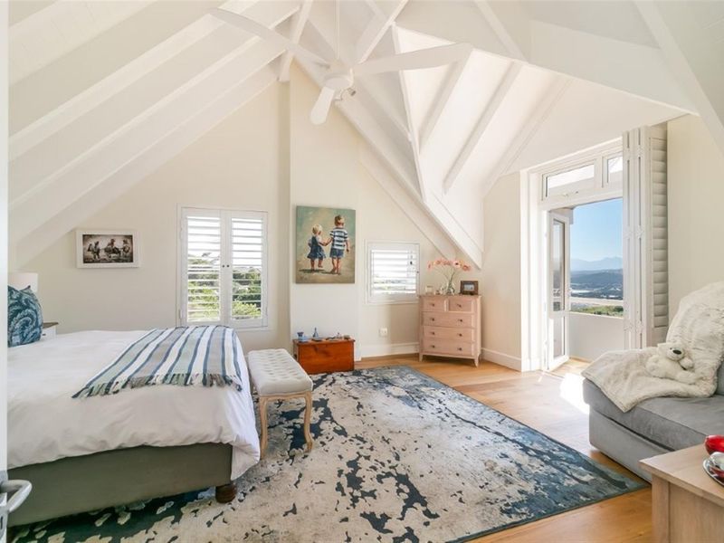 Spacious bedroom featuring a high vaulted ceiling with exposed rafters, hardwood flooring, plantation shutters, and direct access to a private balcony with scenic views.