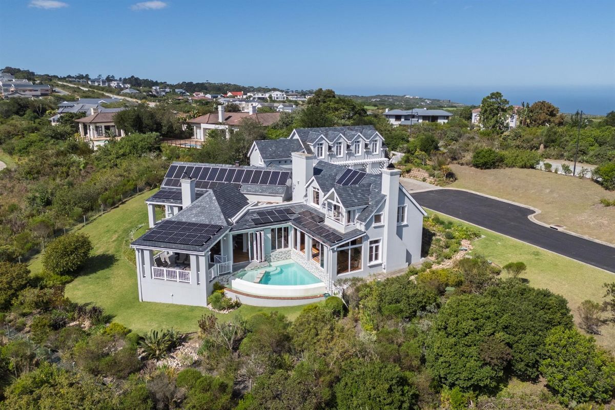 Aerial view of a large residential property featuring a swimming pool, extensive solar panel installation, and a well-maintained garden in a coastal setting.