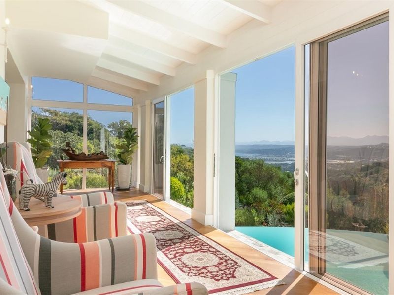 A bright, sun-filled enclosed patio featuring exposed beam ceilings, hardwood floors, and expansive sliding glass doors offering panoramic views of the landscape and pool.