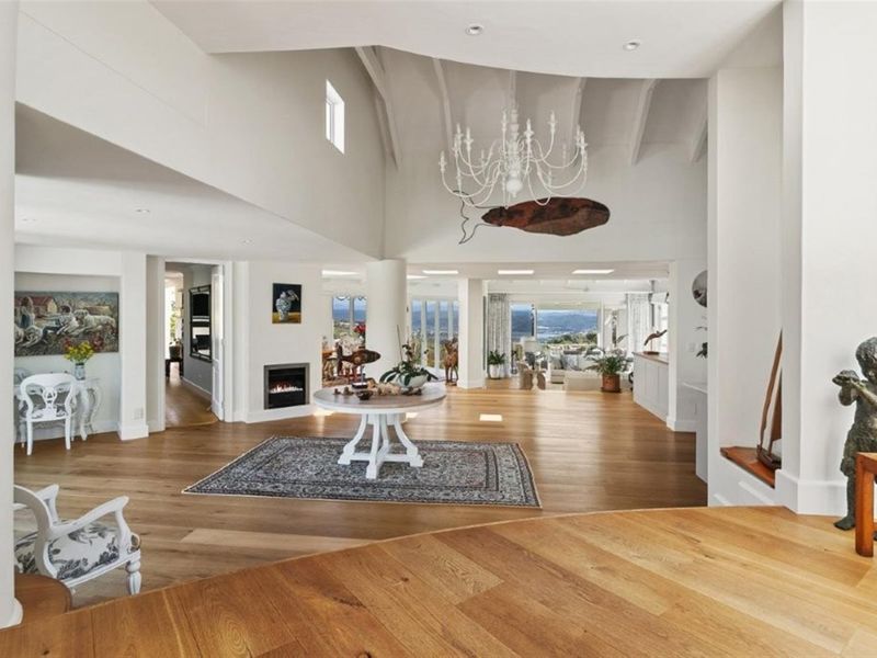 Spacious open-plan living area featuring high vaulted ceilings with exposed beams, hardwood flooring, and a modern built-in fireplace.