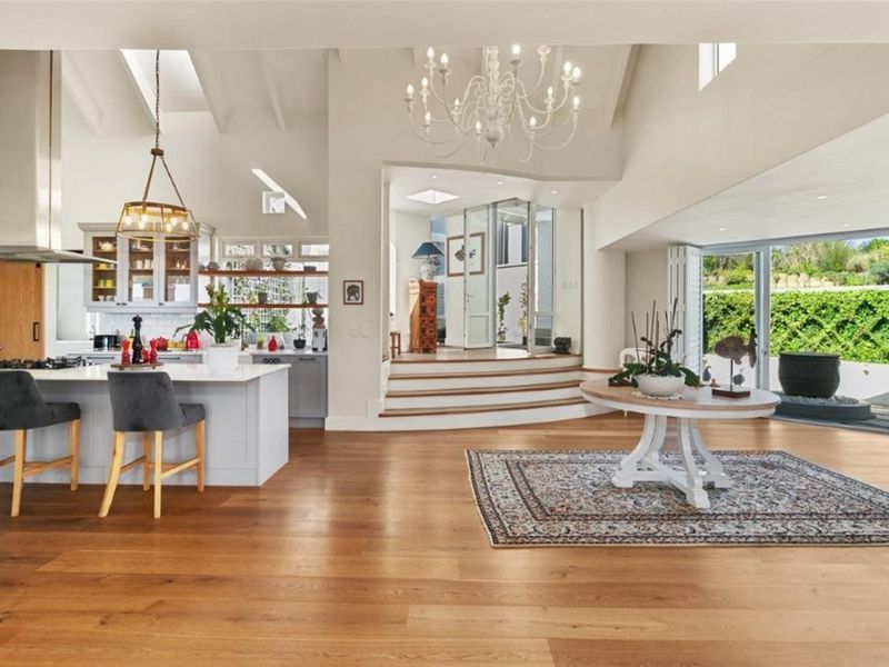 Spacious open-plan living area featuring a modern kitchen with island, vaulted ceilings with skylights, and seamless flow to the outdoor patio through bi-fold doors.