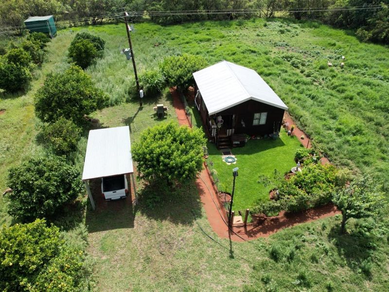 Aerial view of a rural property featuring a main dwelling with a metal roof, a detached carport, and a landscaped garden area.