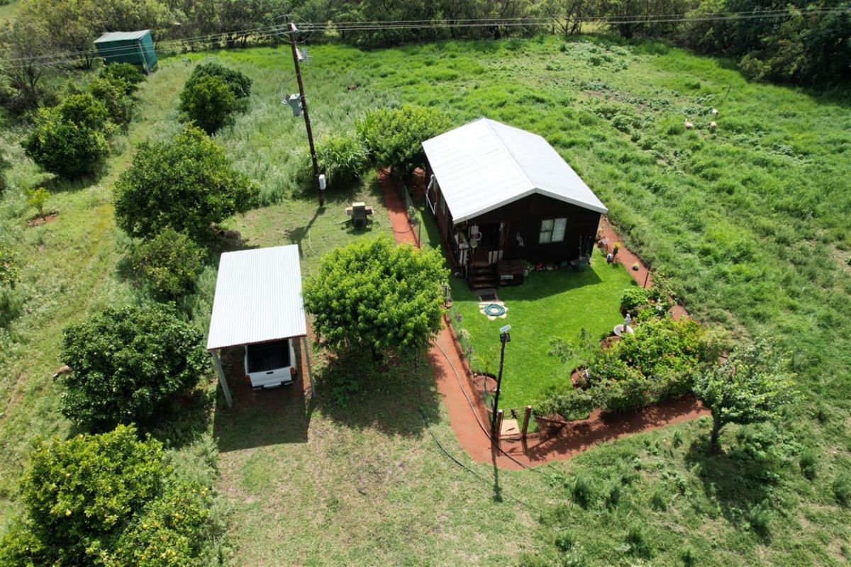 Aerial view of a rural property featuring a main dwelling with a metal roof, a detached carport, and a landscaped garden area.