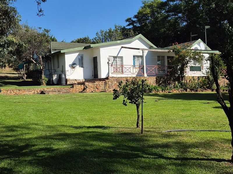 Rear view of a farm-style residence featuring stone cladding, a tiled roof, and a spacious garden area.