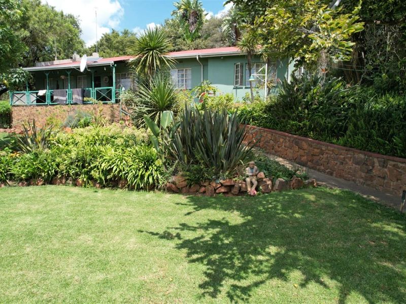 A rear view of the farmhouse featuring a covered patio, stone retaining walls, and a well-established garden setting.
