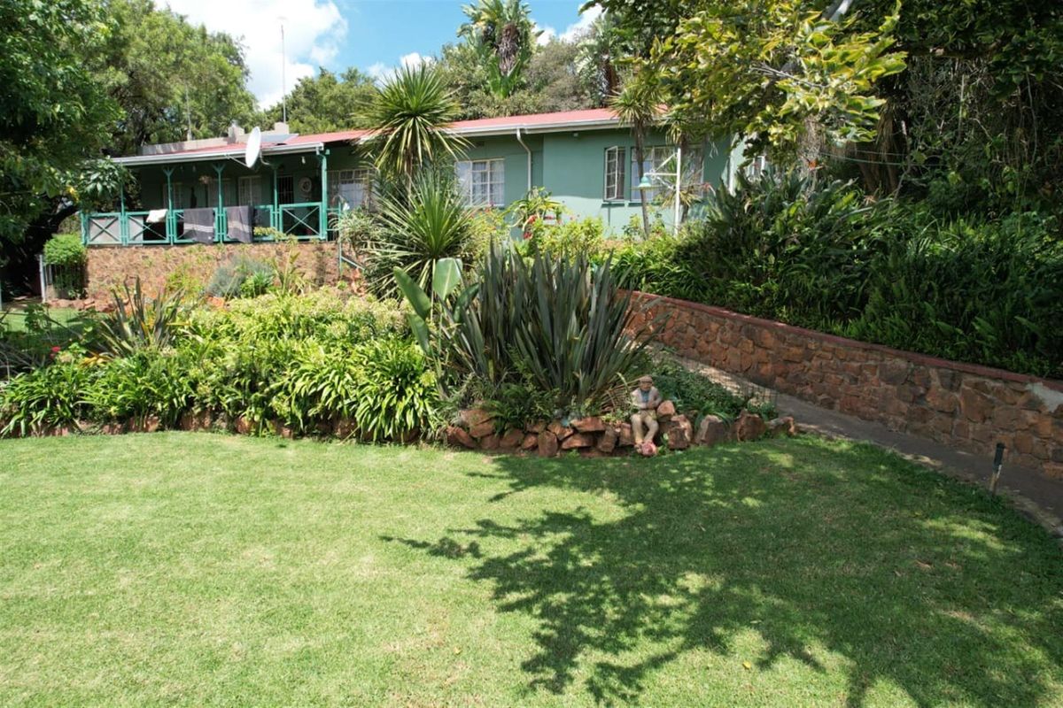 A rear view of the farmhouse featuring a covered patio, stone retaining walls, and a well-established garden setting.