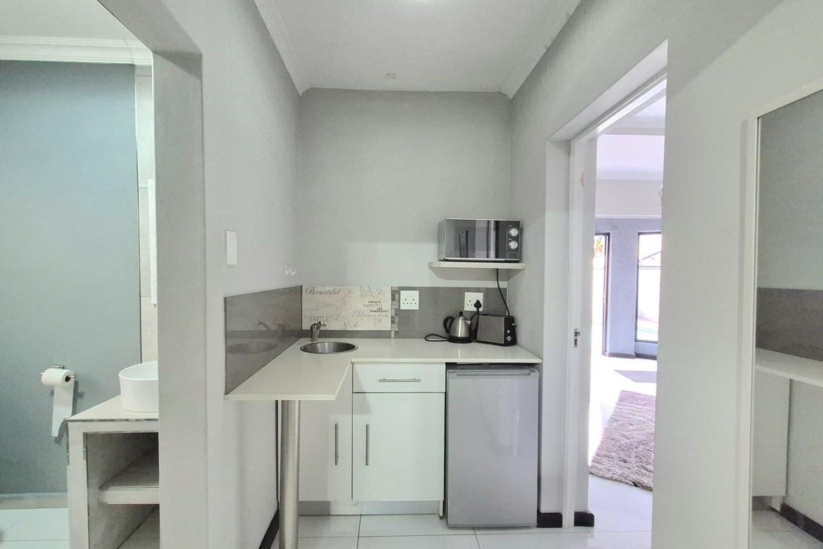 A compact kitchenette featuring white cabinetry, a small sink, and tiled surfaces, conveniently positioned adjacent to a bathroom and living area.