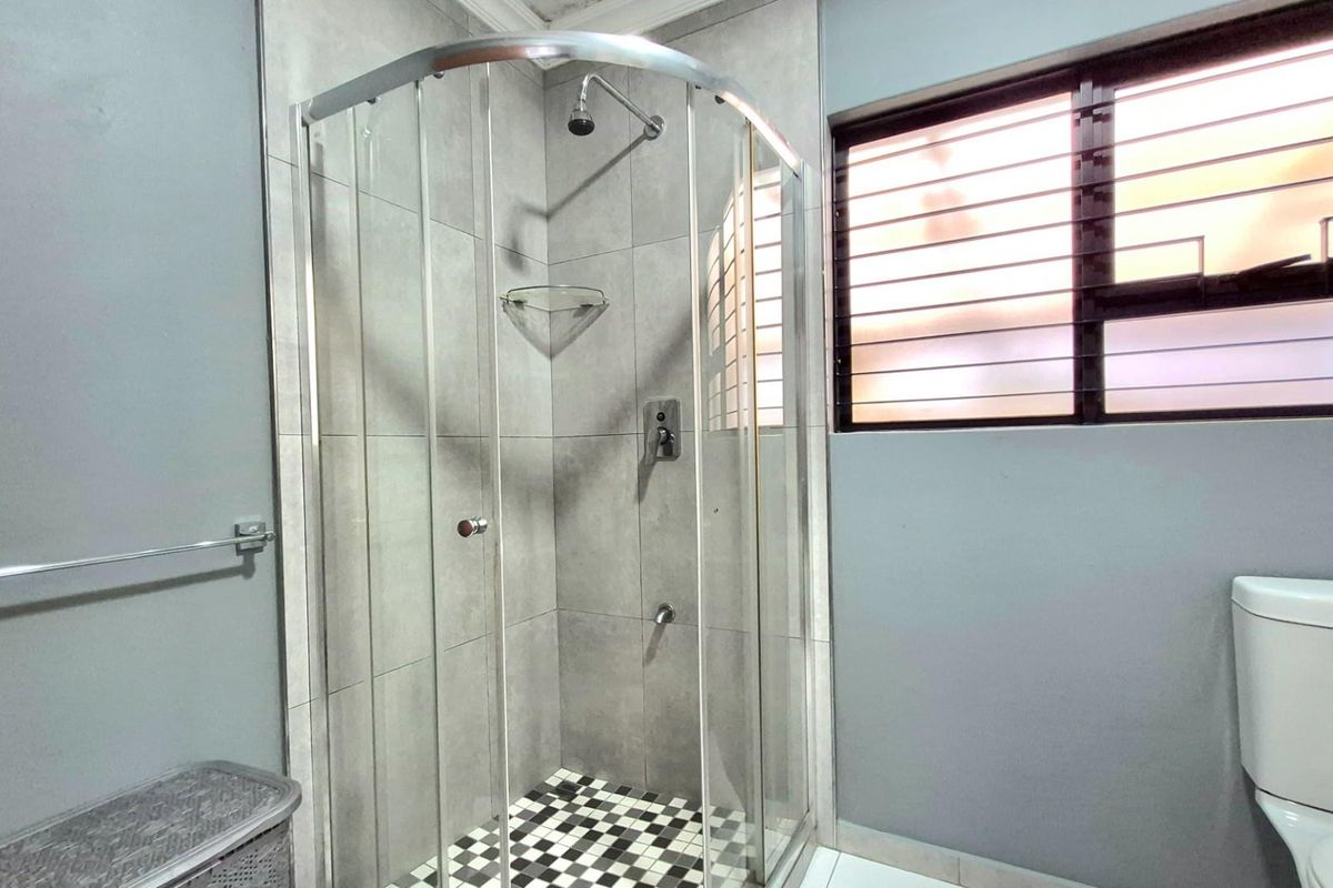 A modern bathroom featuring a curved glass shower enclosure with tiled walls, checkered flooring, and a window with security bars.