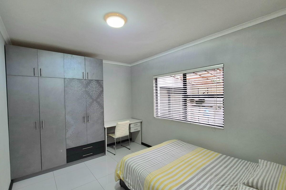 A well-maintained bedroom featuring modern built-in cupboards, tiled flooring, and venetian blinds, offering a clean and functional living space.