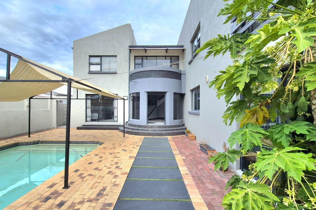 Rear exterior view of the guest house featuring a swimming pool, paved patio area with a shade sail, and modern architectural design.