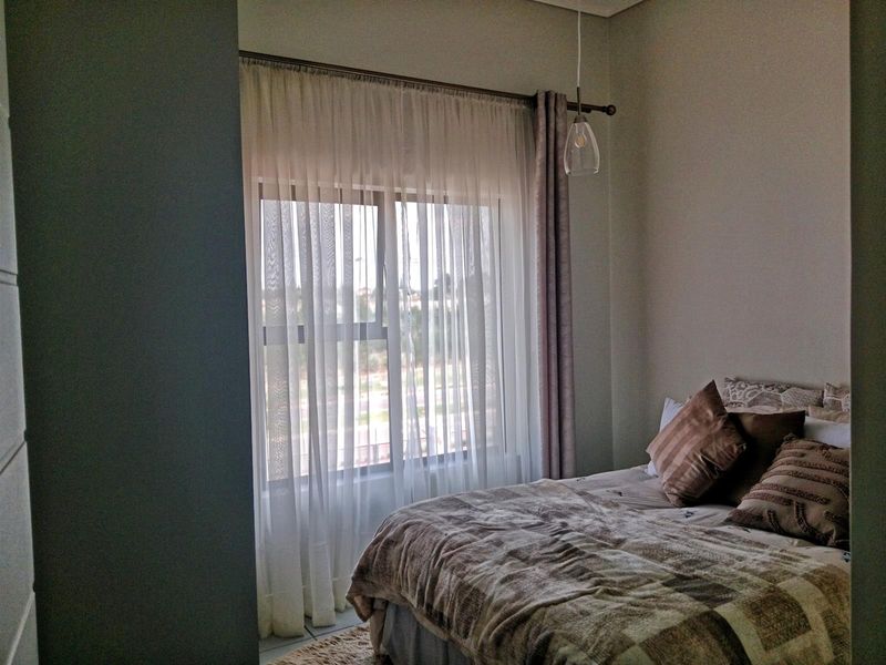 A cozy bedroom featuring a large window with sheer curtains and a modern pendant light fixture.