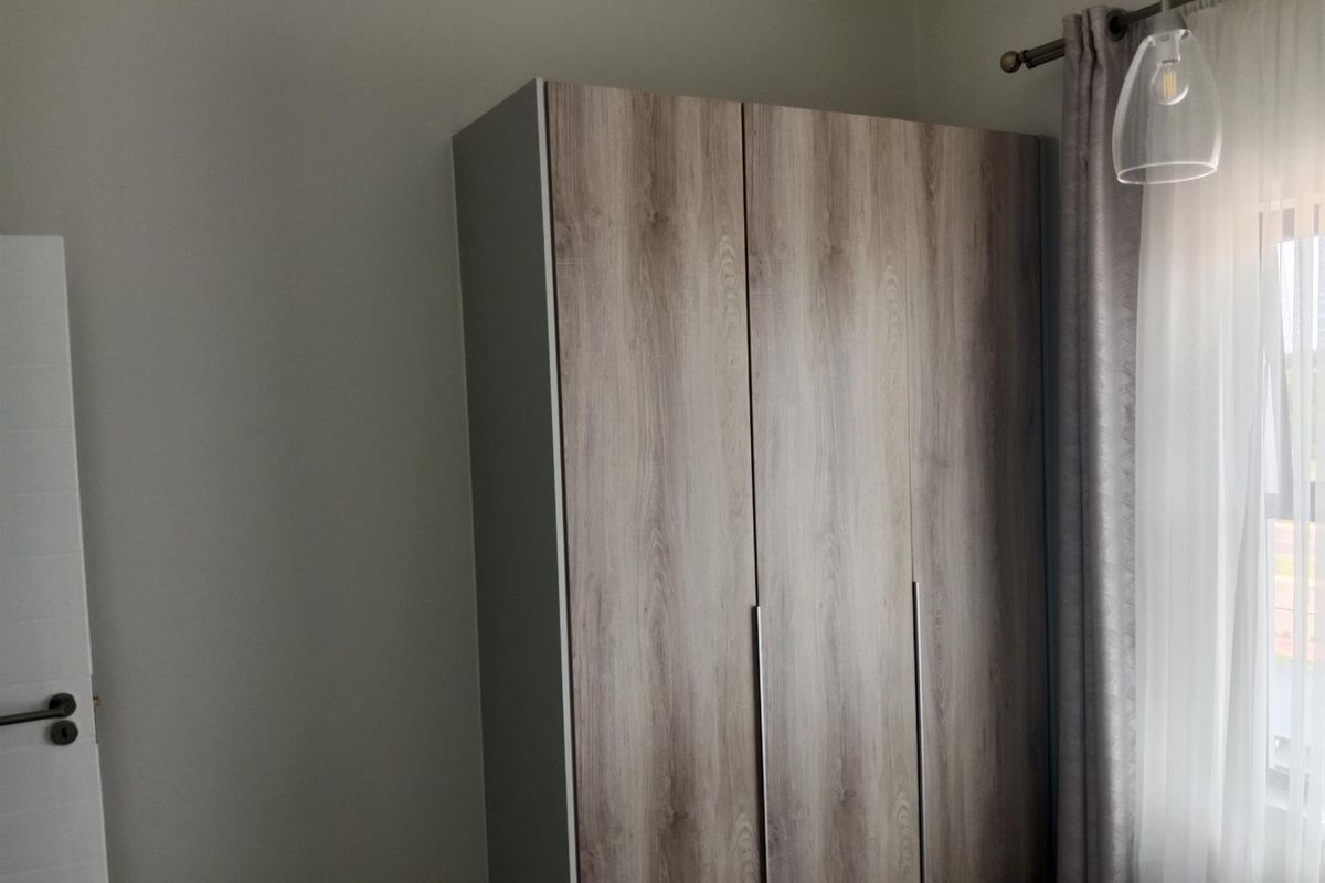 A bedroom featuring a modern wood-finish built-in wardrobe, neutral wall tones, and a pendant light fixture.