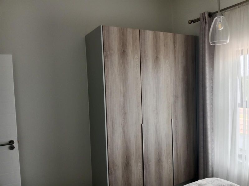 A bedroom featuring a modern wood-finish built-in wardrobe, neutral wall tones, and a pendant light fixture.