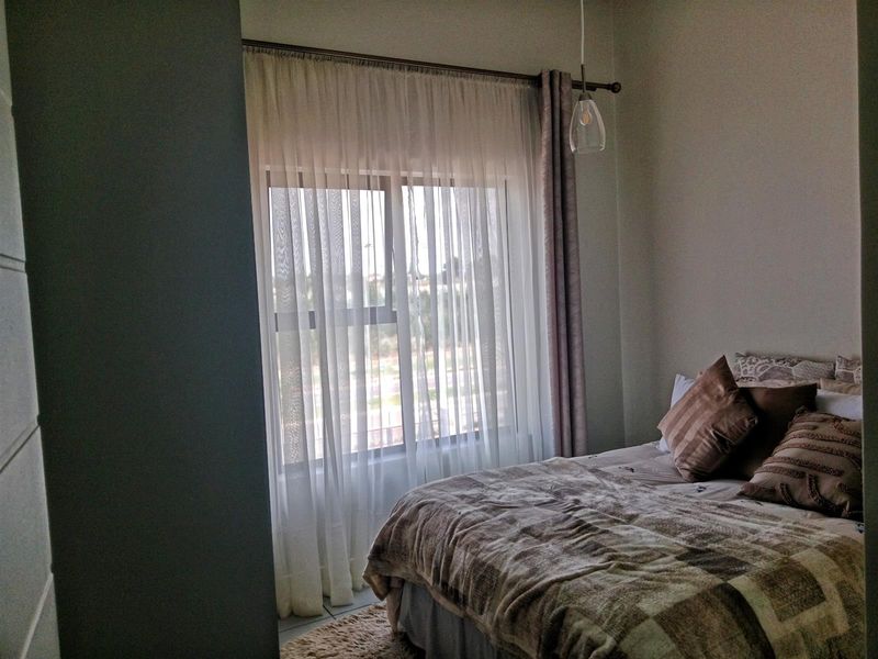 A cozy bedroom featuring a large window with sheer curtains and a modern pendant light fixture.