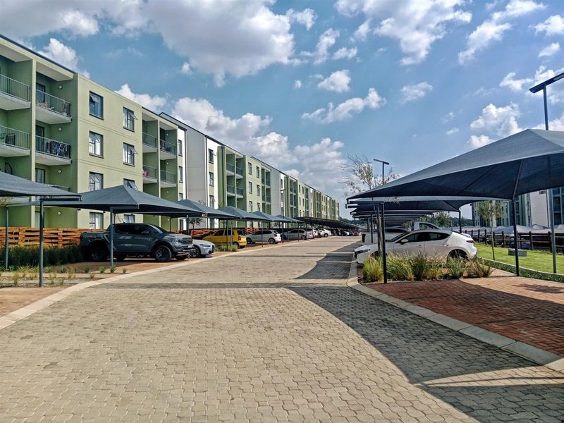 Exterior view of a modern apartment complex featuring paved parking areas with shade cloth carports and multi-story residential units with balconies.