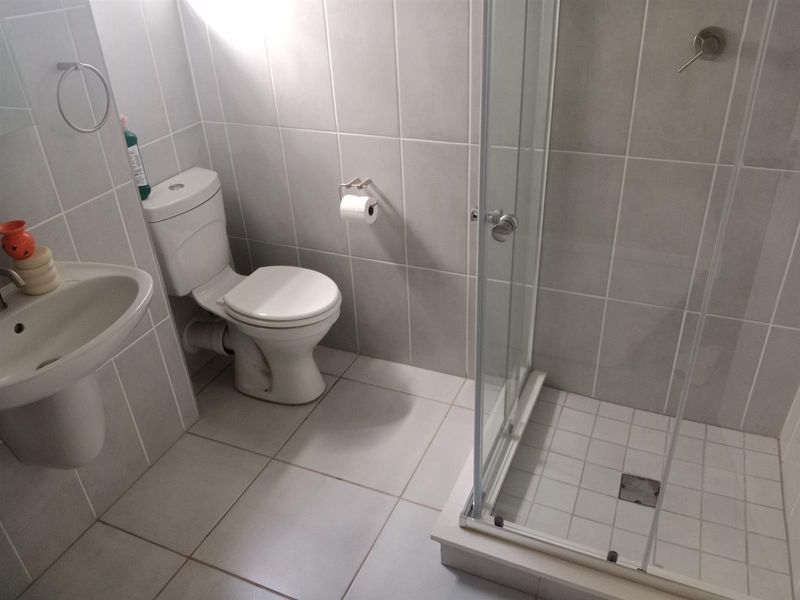 A clean, functional bathroom featuring a pedestal basin, a standard toilet, and a glass-enclosed shower with neutral wall and floor tiling.