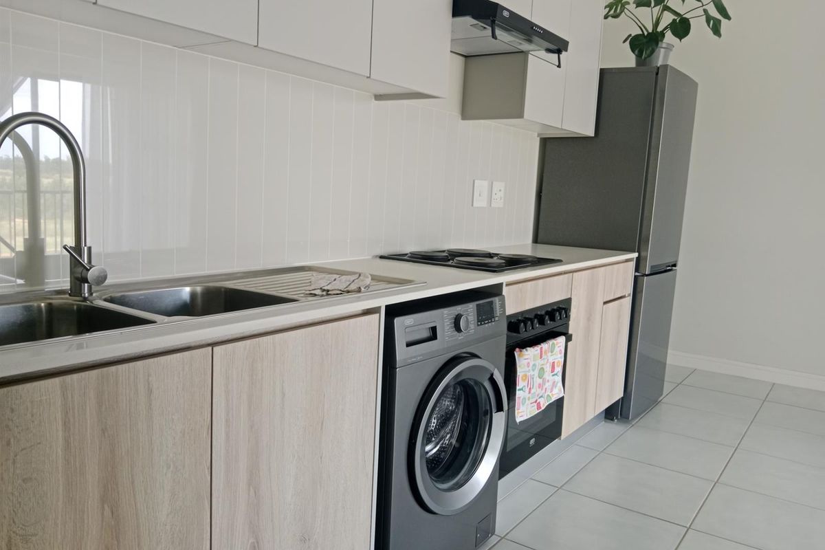 Modern kitchen featuring light wood-look cabinetry, tiled splashback, integrated electric hob, oven, extractor fan, and stainless steel sink with mixer tap.