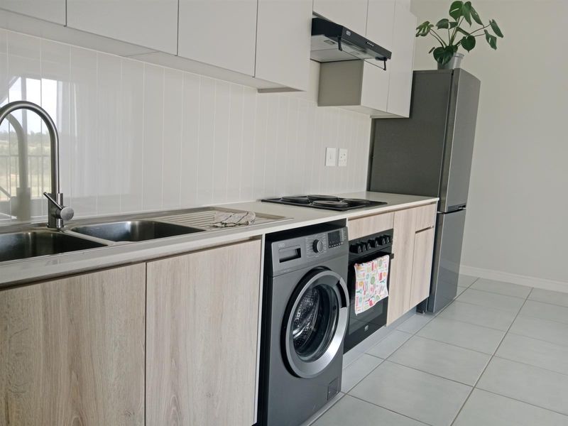 Modern kitchen featuring light wood-look cabinetry, tiled splashback, integrated electric hob, oven, extractor fan, and stainless steel sink with mixer tap.