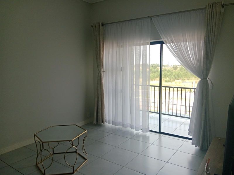 A bright, open-plan living area featuring neutral tiled flooring and a large sliding glass door providing direct access to a private balcony.
