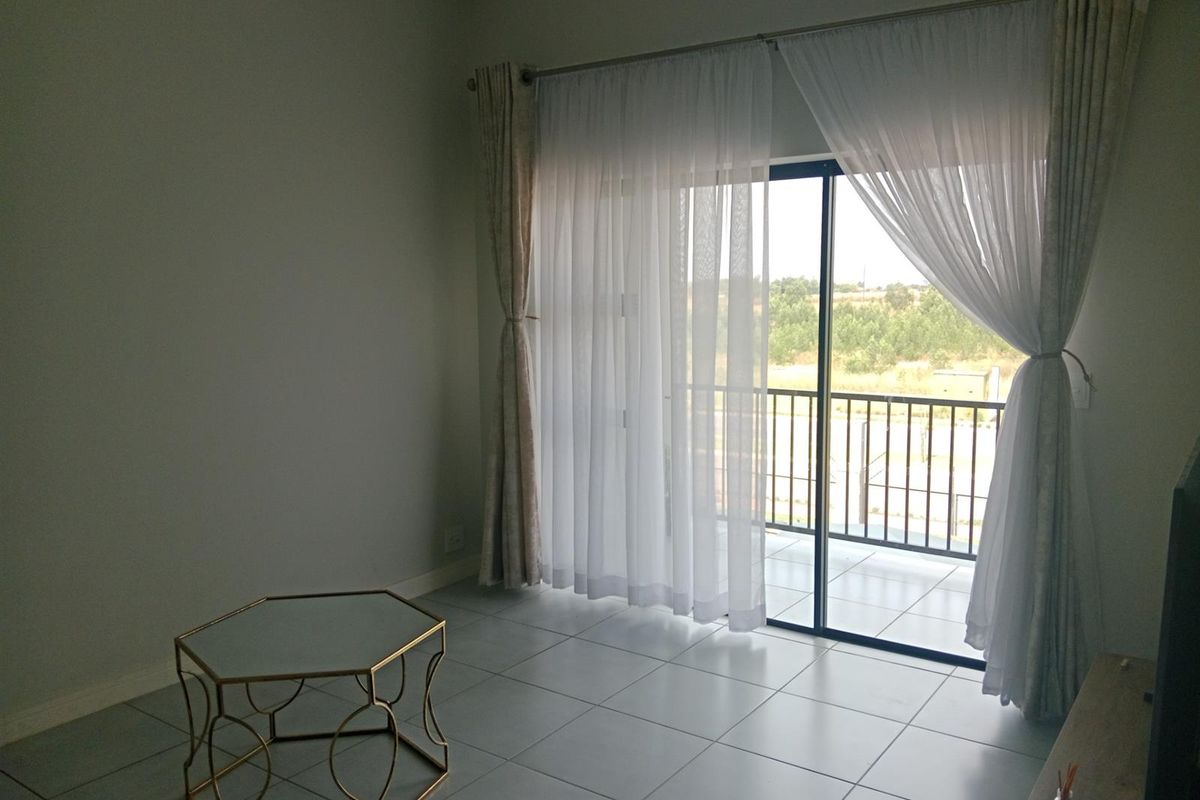 A bright, open-plan living area featuring neutral tiled flooring and a large sliding glass door providing direct access to a private balcony.