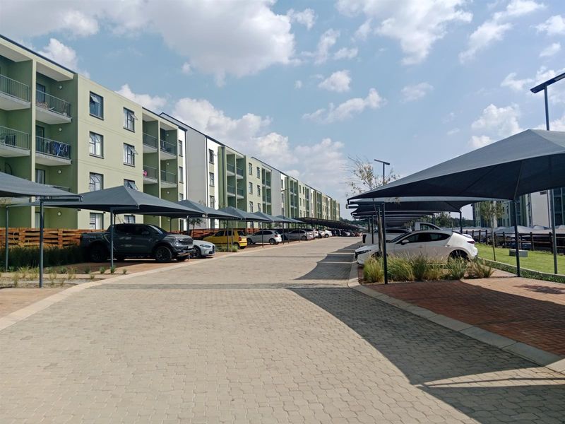 Exterior view of a modern apartment complex featuring paved parking areas with shade cloth carports and multi-story residential buildings with balconies.