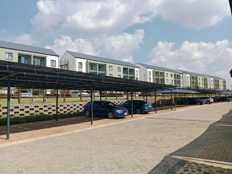 Exterior view of an apartment complex featuring covered parking bays, paved driveways, and multi-story residential buildings with modern architectural finishes.