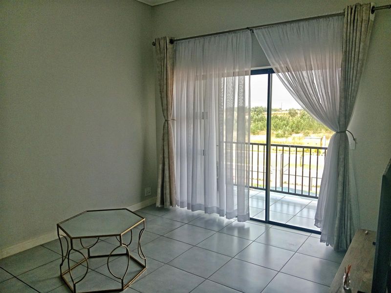 A bright, open-plan living area featuring neutral tiled flooring and a large sliding glass door providing direct access to a private balcony.