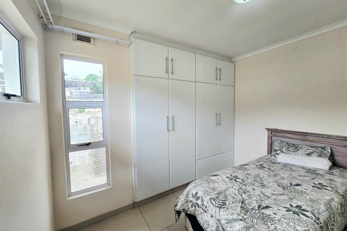 A well-maintained bedroom featuring built-in cupboards, tiled flooring, and large aluminium windows that provide natural light.