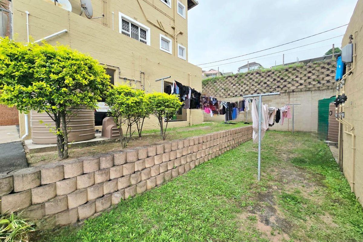 Rear exterior view of the apartment building featuring a small garden area, retaining wall, and water storage tank.