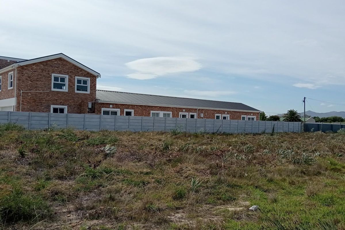 View of the rear of the residential property featuring a brick exterior, metal roofing, and a precast concrete boundary wall bordering the vacant land.