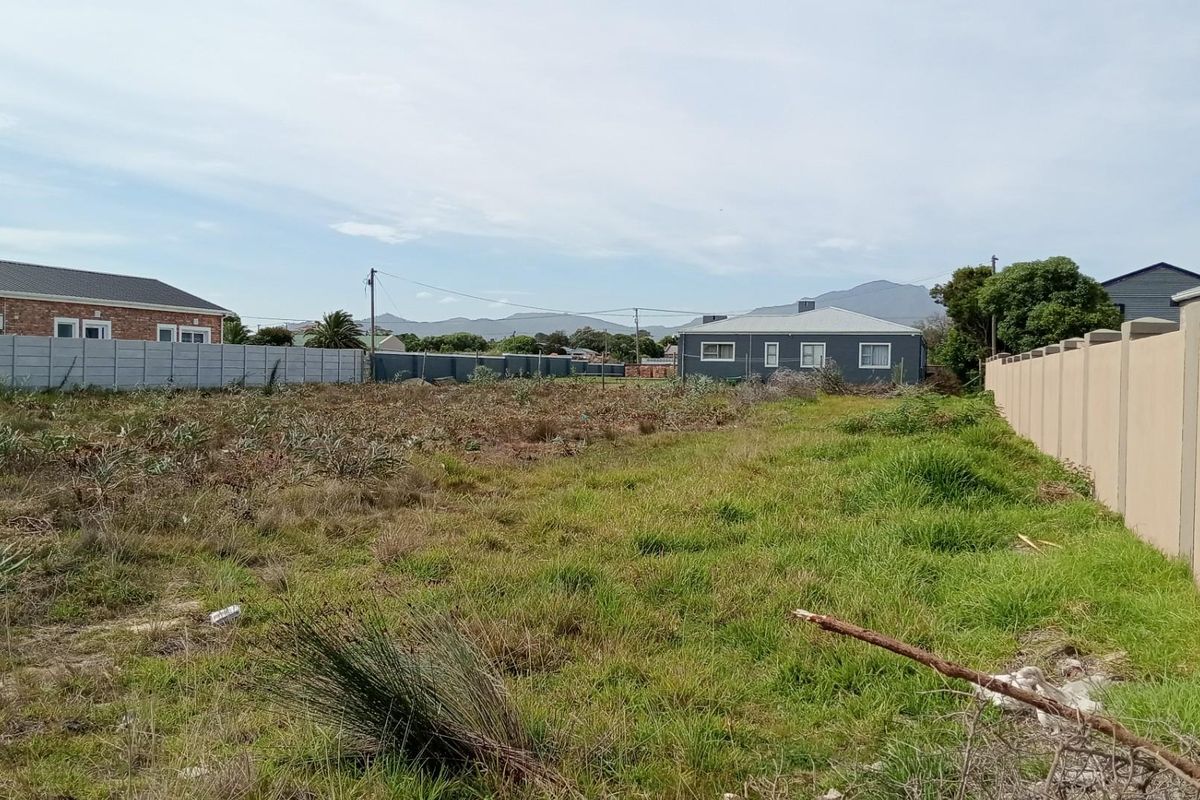 A vacant residential plot featuring established boundary walls on both sides and views of the surrounding neighborhood and distant mountains.