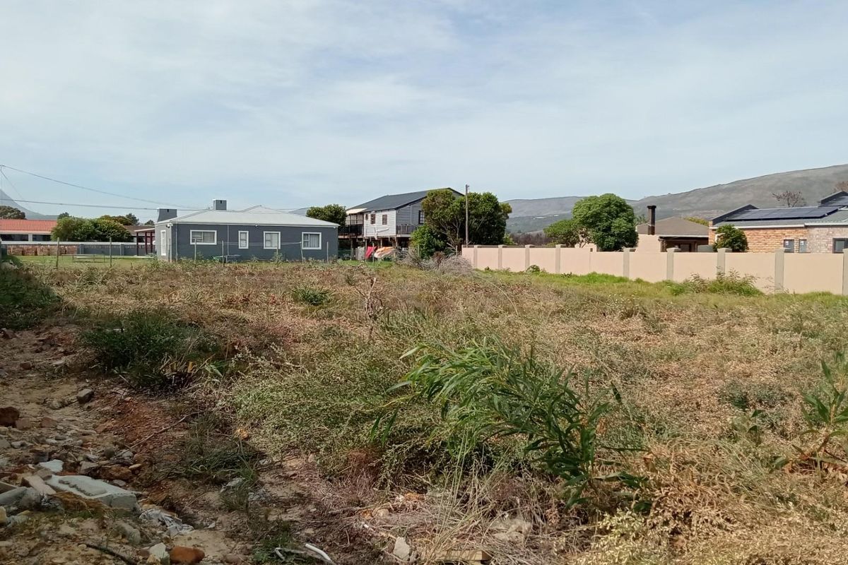 A vacant residential plot featuring boundary walls on both sides, situated in a developed neighborhood with mountain views in the distance.