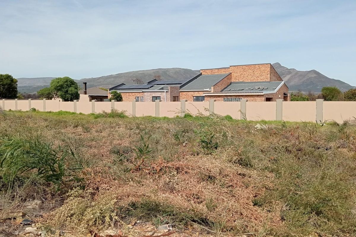 A view of a vacant residential plot with a perimeter wall and neighbouring brick house in the background.