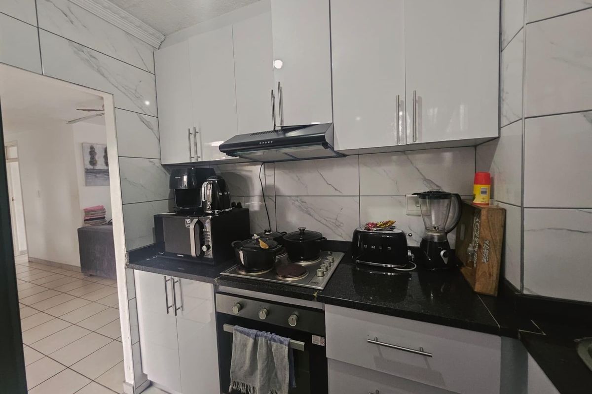 Compact kitchen featuring white gloss cabinetry, black granite countertops, built-in oven, electric hob, extractor fan, and modern marble-look wall tiling.