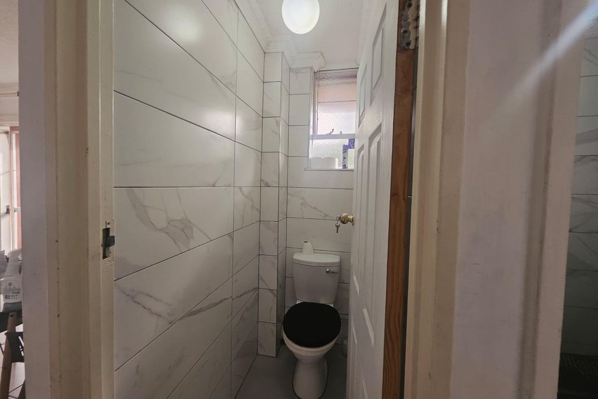 A compact bathroom featuring modern marble-look wall tiles, tiled flooring, and a standard toilet, providing a clean and functional space.