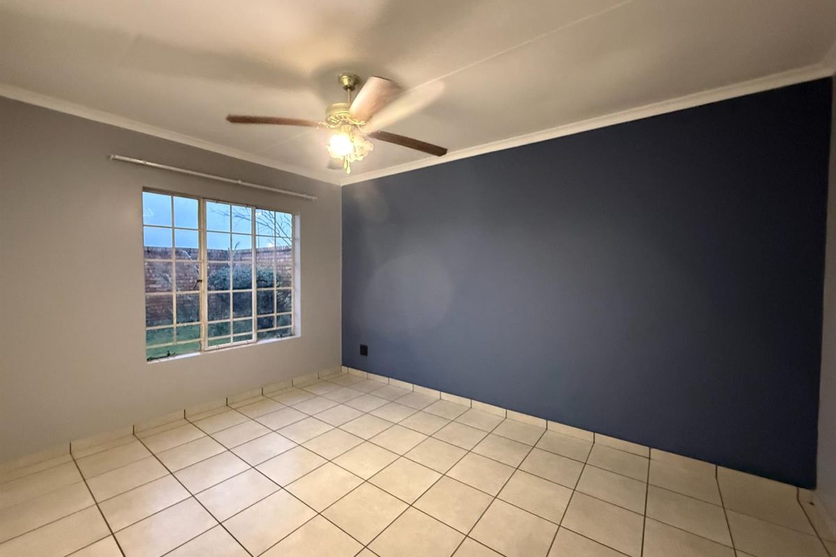 An empty bedroom featuring tiled flooring, a ceiling fan, and a large grid-pattern window with a view of the exterior brick wall.