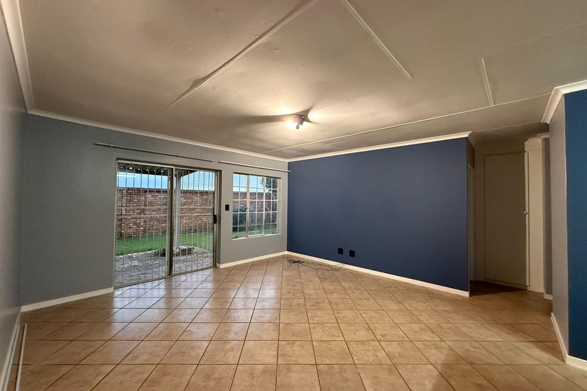 Spacious, empty living area featuring ceramic tiled flooring, a sliding glass door with security gate, and a bold blue accent wall.