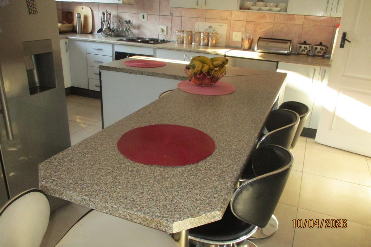 Functional kitchen featuring a central breakfast bar, laminate countertops, white cabinetry, and tiled flooring, offering a practical layout for daily meal preparation.