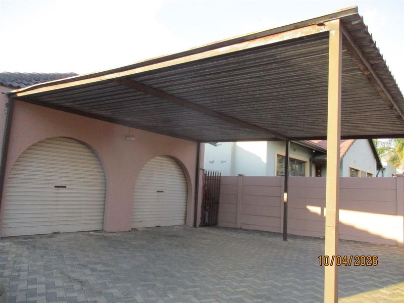 A paved driveway area featuring a double carport structure and two arched garage doors with roller shutters.