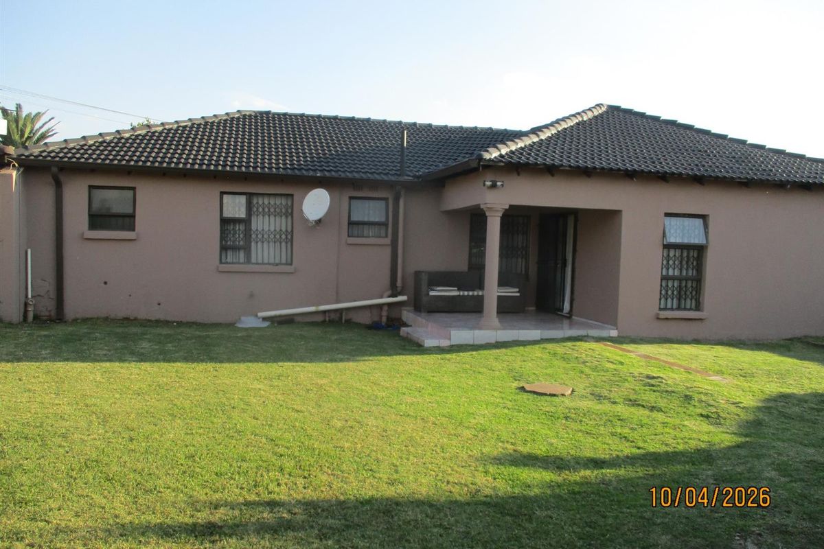 Rear view of the house featuring a tiled roof, covered patio area, and a spacious lawn.