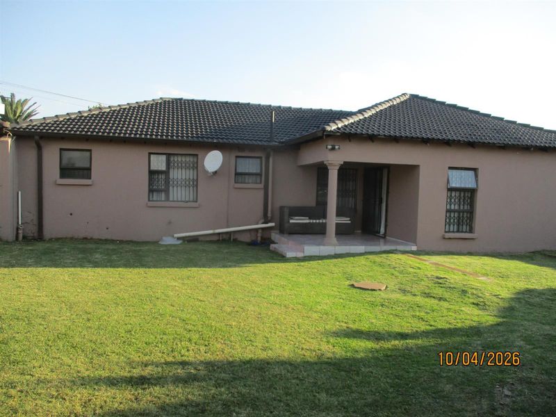 Rear view of the house featuring a tiled roof, covered patio area, and a spacious lawn.